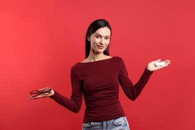 Photo of Woman choosing between glasses and contact lenses on red background