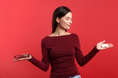 Photo of Woman choosing between glasses and contact lenses on red background