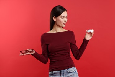 Photo of Woman choosing between glasses and contact lenses on red background