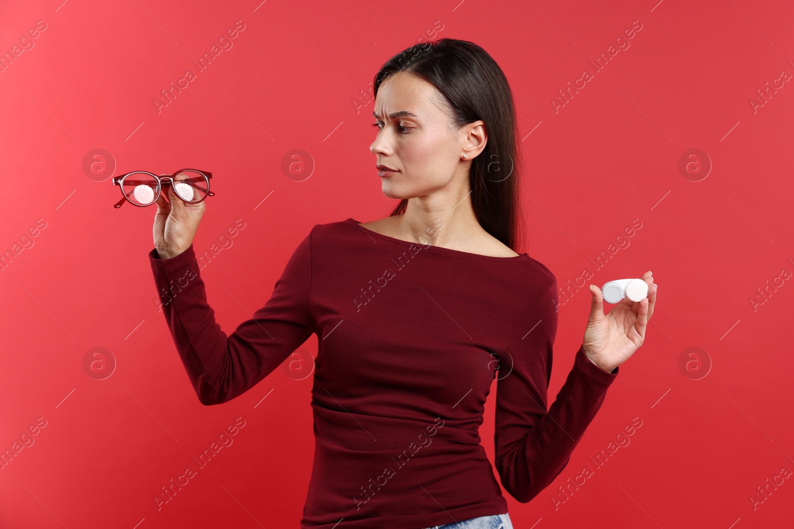 Photo of Woman choosing between glasses and contact lenses on red background