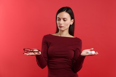 Photo of Woman choosing between glasses and contact lenses on red background