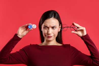 Photo of Woman choosing between glasses and contact lenses on red background
