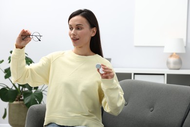 Photo of Woman choosing between glasses and contact lenses on sofa indoors, space for text