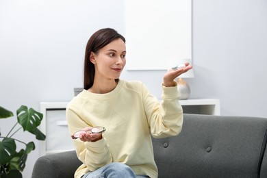 Photo of Woman choosing between glasses and contact lenses on sofa indoors