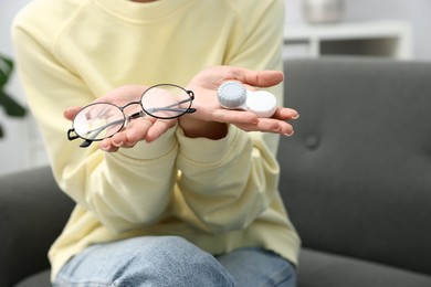 Photo of Woman choosing between glasses and contact lenses on sofa indoors, closeup. Space for text