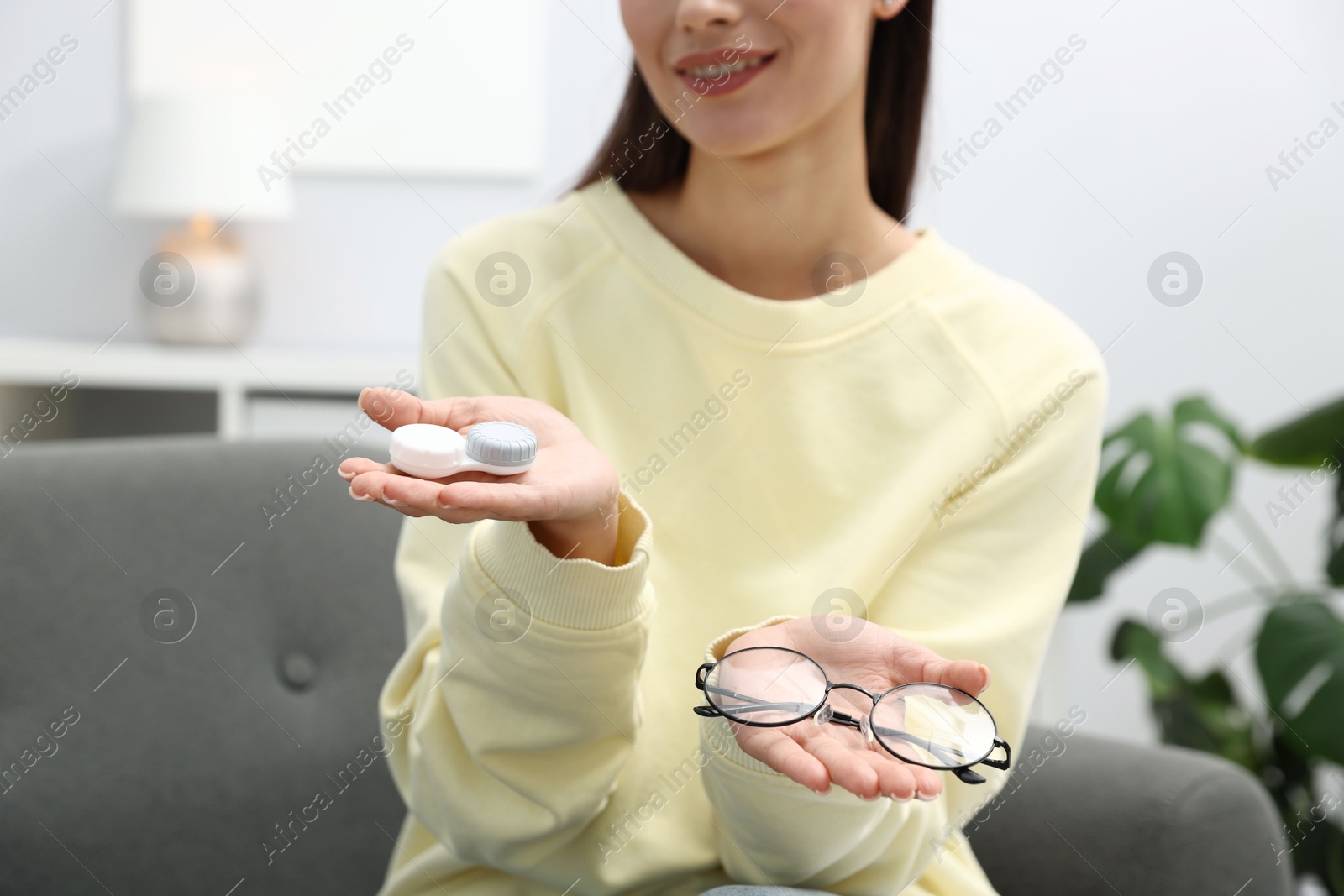 Photo of Woman choosing between glasses and contact lenses on sofa indoors, closeup