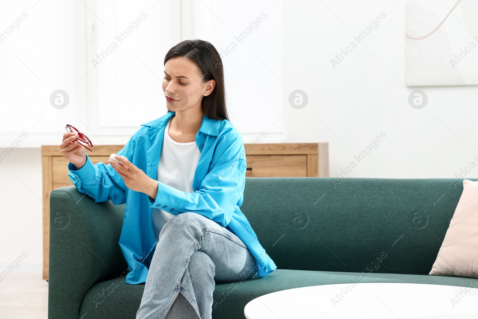 Photo of Woman choosing between glasses and contact lenses on sofa indoors, space for text