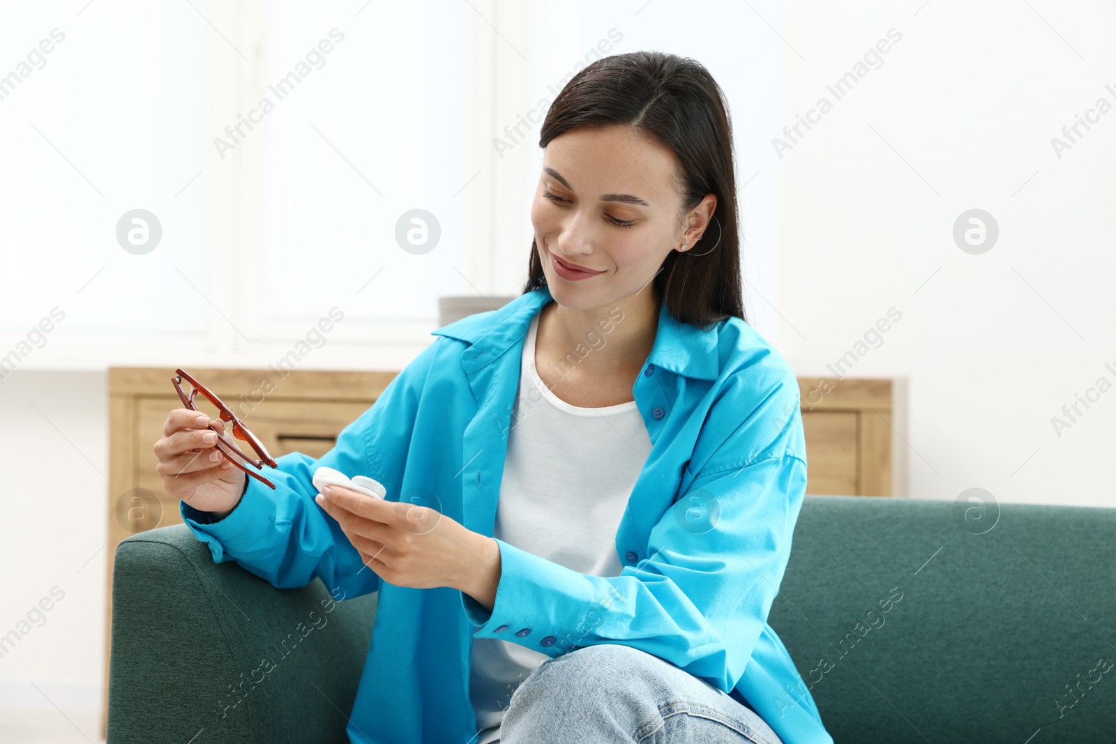 Photo of Woman choosing between glasses and contact lenses on sofa indoors
