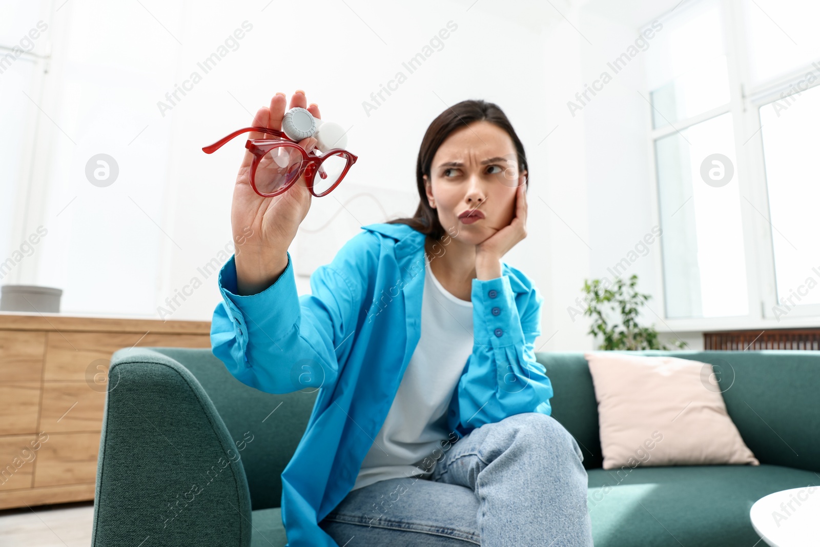 Photo of Woman choosing between glasses and contact lenses on sofa indoors
