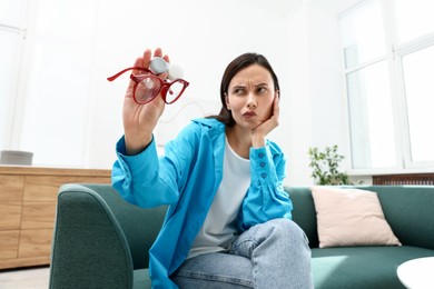 Photo of Woman choosing between glasses and contact lenses on sofa indoors