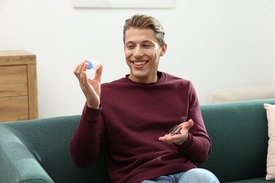 Photo of Man choosing between glasses and contact lenses on sofa indoors