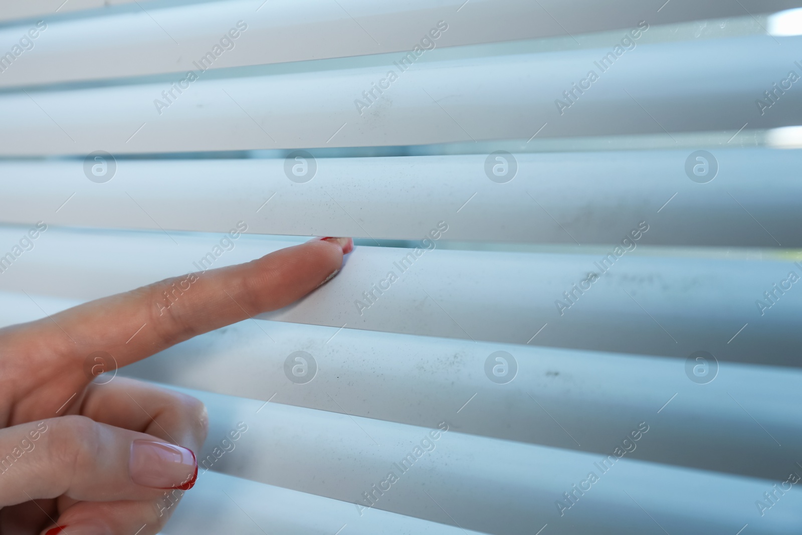 Photo of Woman swiping dust from window blinds indoors, closeup