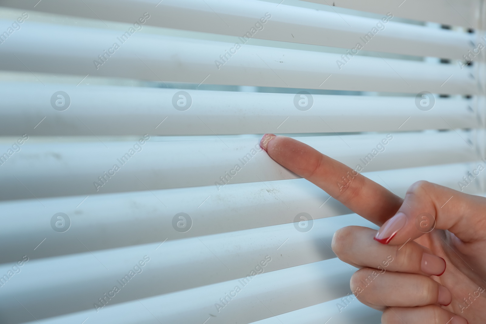 Photo of Woman swiping dust from window blinds indoors, closeup