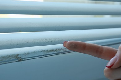 Photo of Woman showing dust from window blinds indoors, closeup