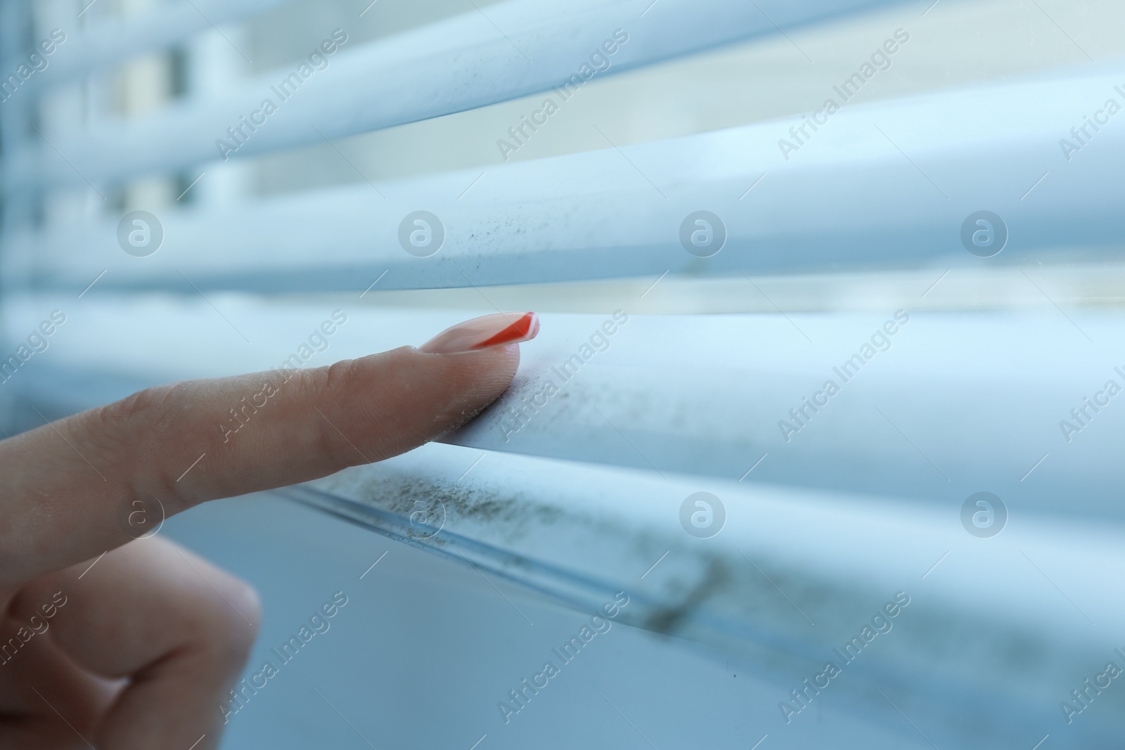 Photo of Woman swiping dust from window blinds indoors, closeup