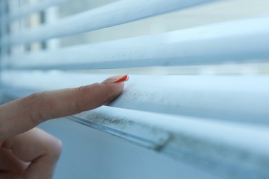 Photo of Woman swiping dust from window blinds indoors, closeup