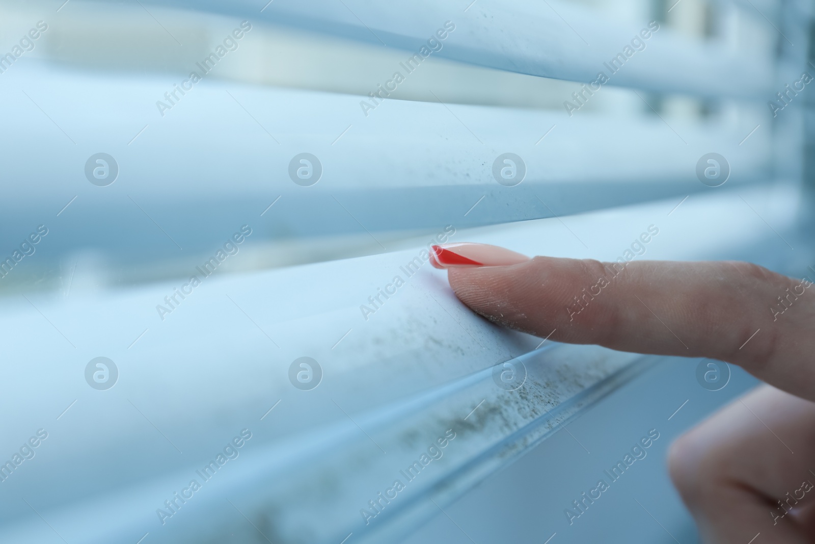 Photo of Woman swiping dust from window blinds indoors, closeup