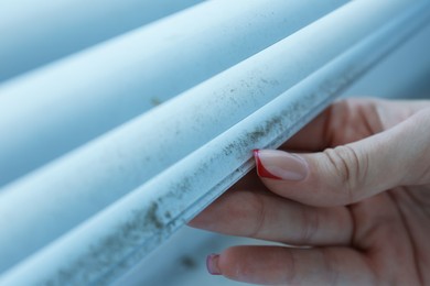 Photo of Woman swiping dust from window blinds indoors, closeup