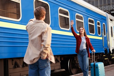 Photo of Goodbye. Man waving to his girlfriend near train outdoors