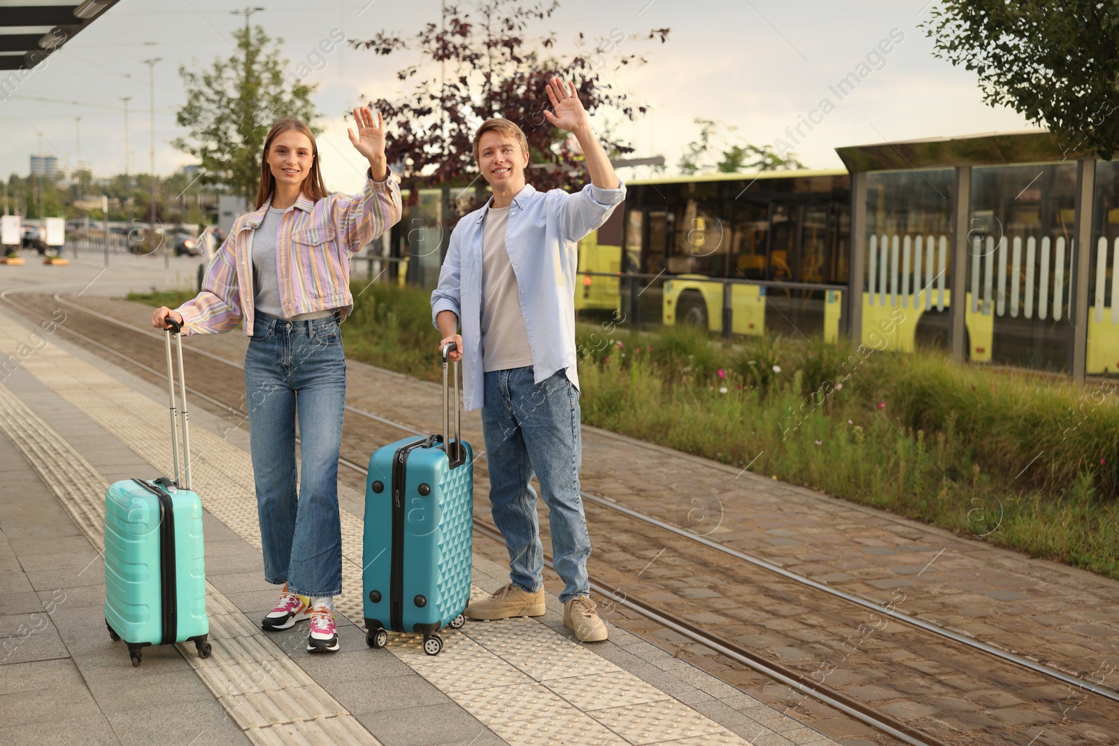 Photo of Goodbye. Lovely couple with suitcases waving at bus stop, space for text
