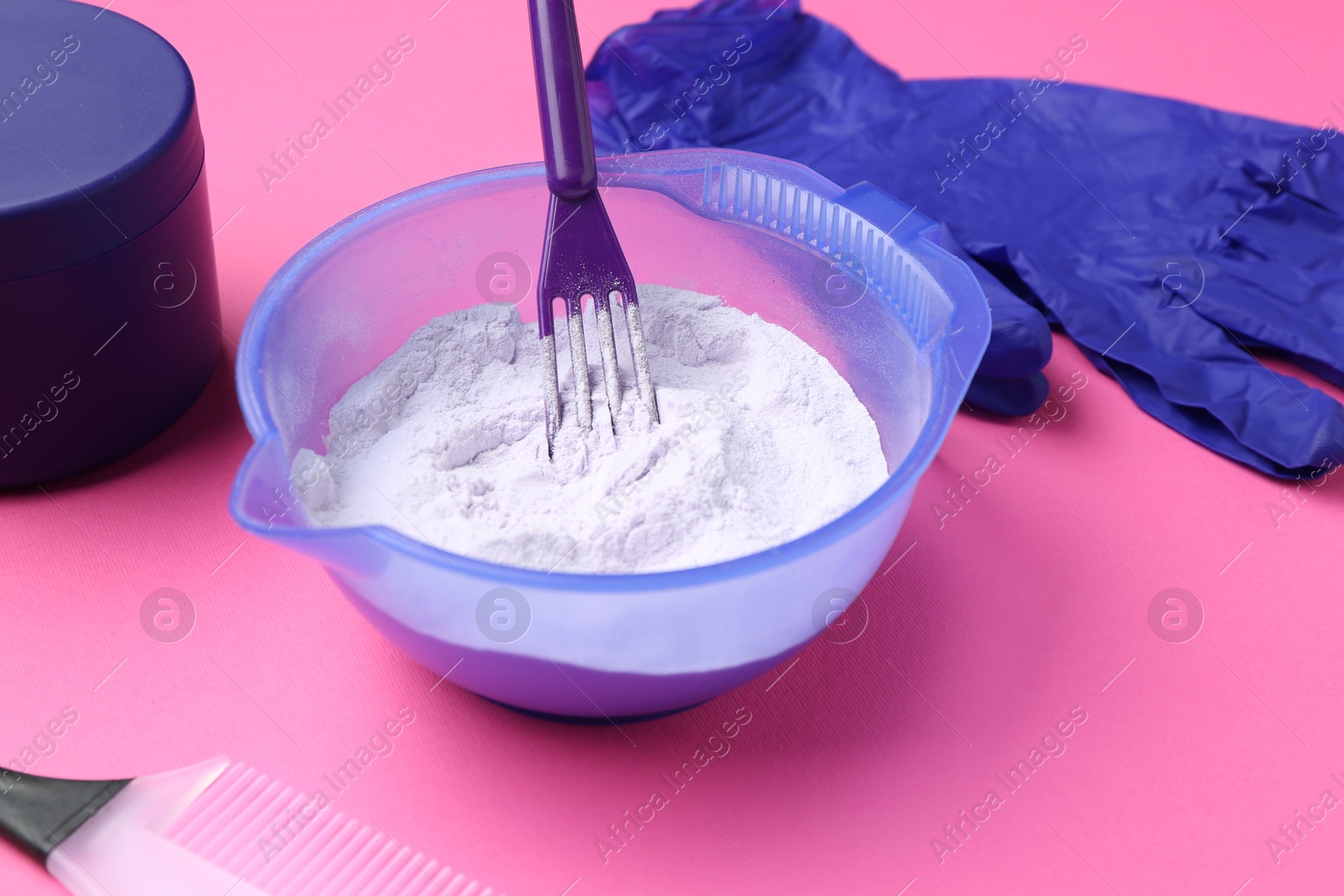Photo of Care cosmetic product for blonde hair in bowl and hairdresser's tools on pink background, closeup