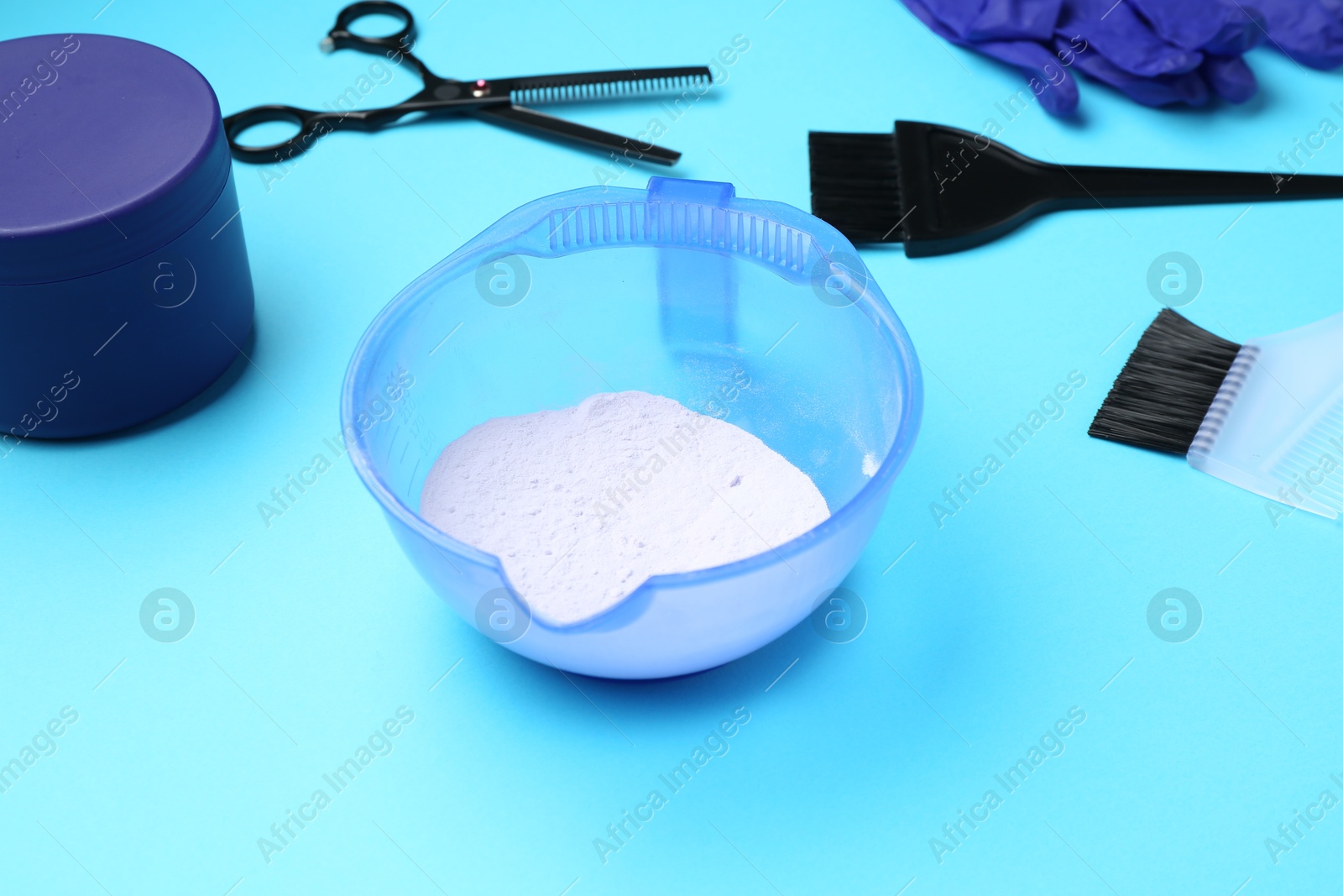 Photo of Care cosmetic product for blonde hair in bowl and hairdresser's tools on light blue background, closeup