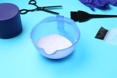 Photo of Care cosmetic product for blonde hair in bowl and hairdresser's tools on light blue background, closeup