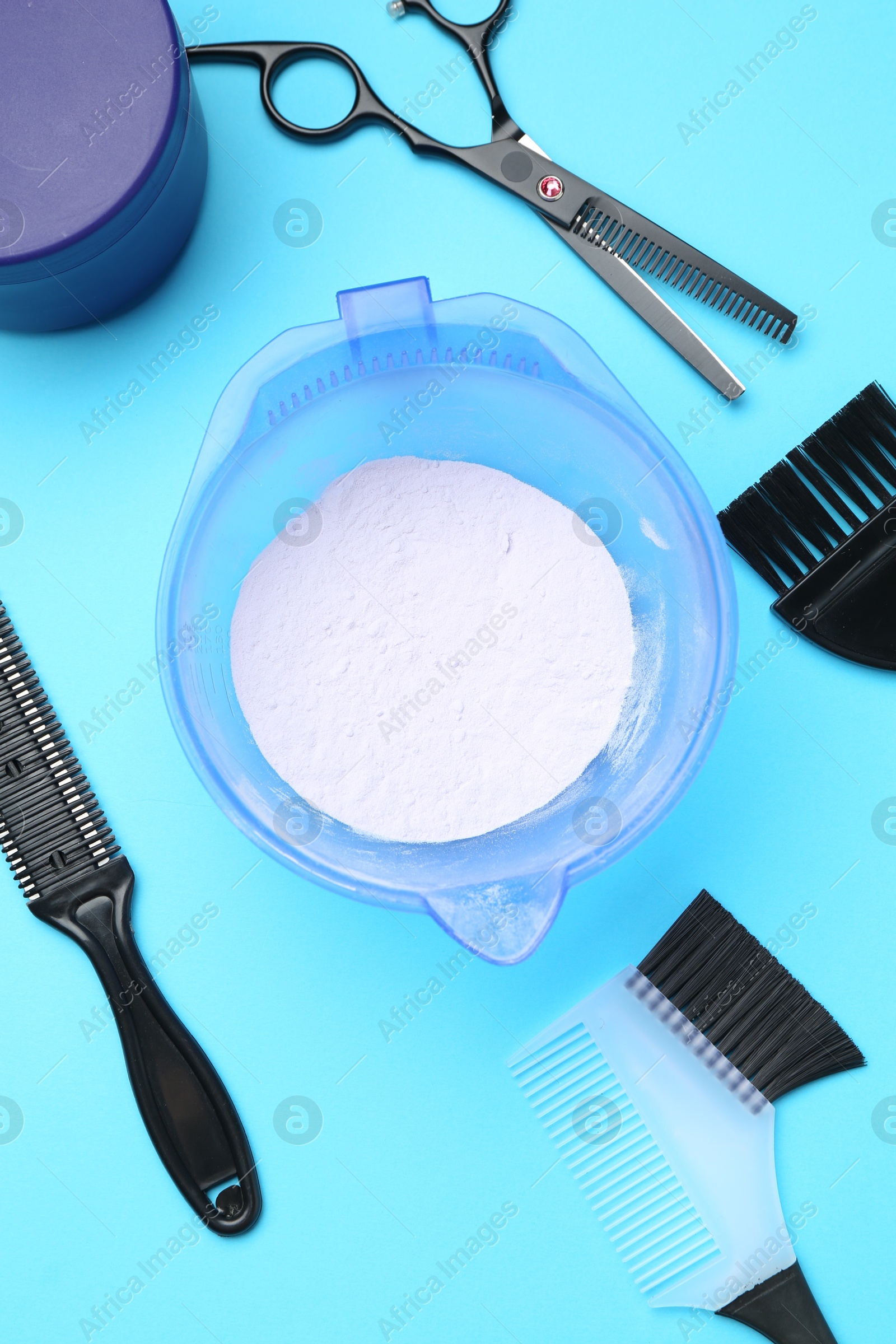 Photo of Care cosmetic product for blonde hair in bowl and hairdresser's tools on light blue background, flat lay