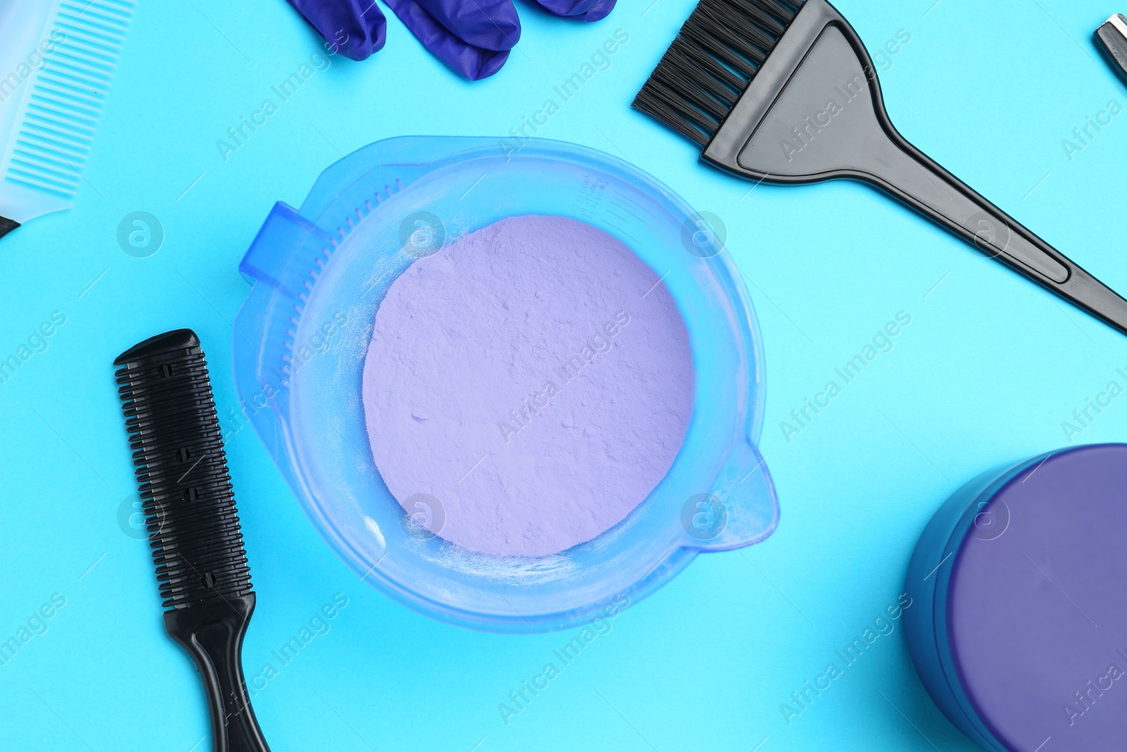 Photo of Care cosmetic product for blonde hair in bowl and hairdresser's tools on light blue background, flat lay