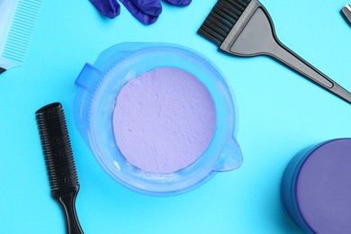 Photo of Care cosmetic product for blonde hair in bowl and hairdresser's tools on light blue background, flat lay