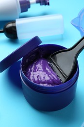 Photo of Care cosmetic product for blonde hair in jar and hairdresser's tools on light blue background, closeup