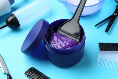 Photo of Care cosmetic product for blonde hair in jar and hairdresser's tools on light blue background, closeup