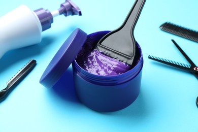 Photo of Care cosmetic product for blonde hair in jar and hairdresser's tools on light blue background, closeup