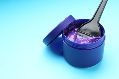Photo of Care cosmetic product for blonde hair in jar and brush on light blue background, closeup. Space for text