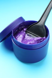 Photo of Care cosmetic product for blonde hair in jar and brush on light blue background, closeup