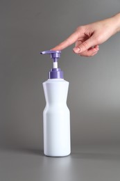 Photo of Woman with bottle of hair care product for blonde hair on grey background, closeup
