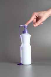 Photo of Woman with bottle of hair care product for blonde hair on grey background, closeup