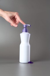 Photo of Woman with bottle of hair care product for blonde hair on grey background, closeup