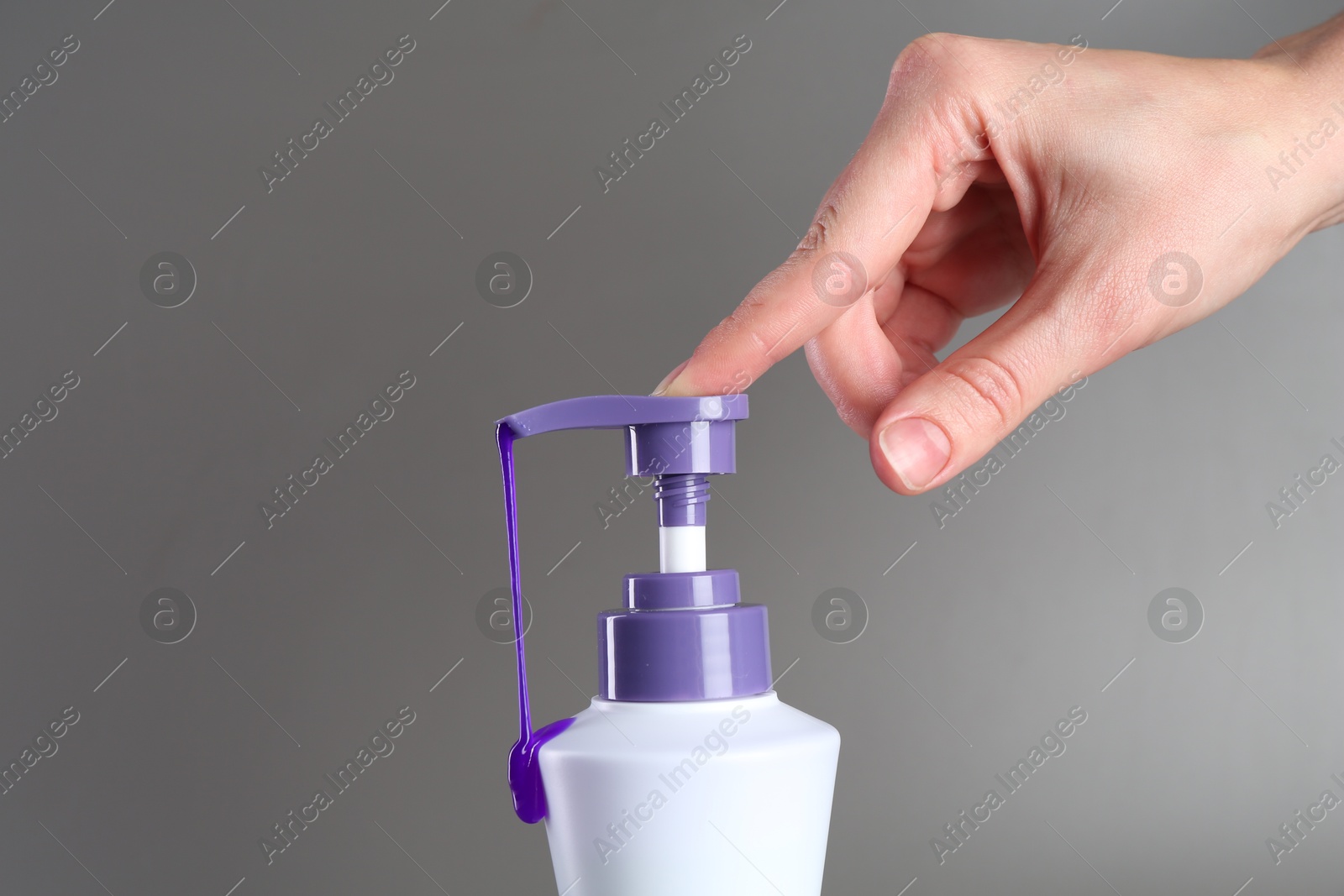 Photo of Woman with bottle of hair care product for blonde hair on grey background, closeup. Space for text
