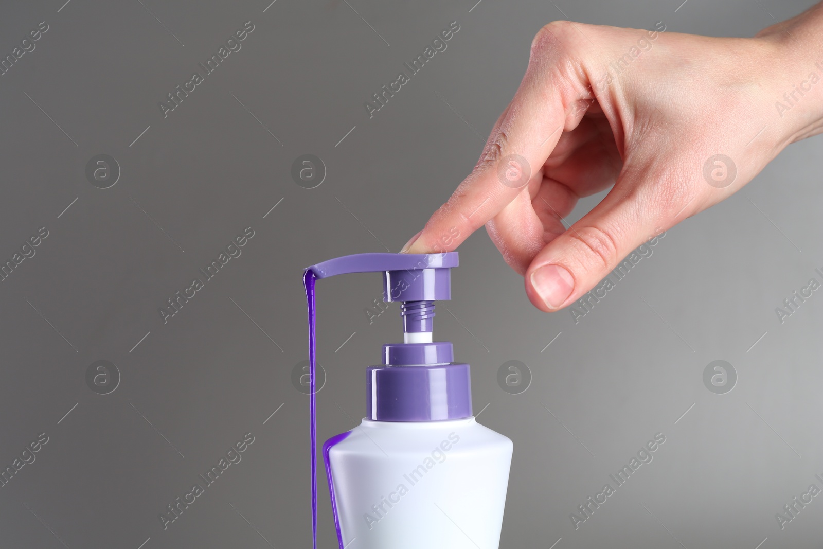 Photo of Woman with bottle of hair care product for blonde hair on grey background, closeup. Space for text