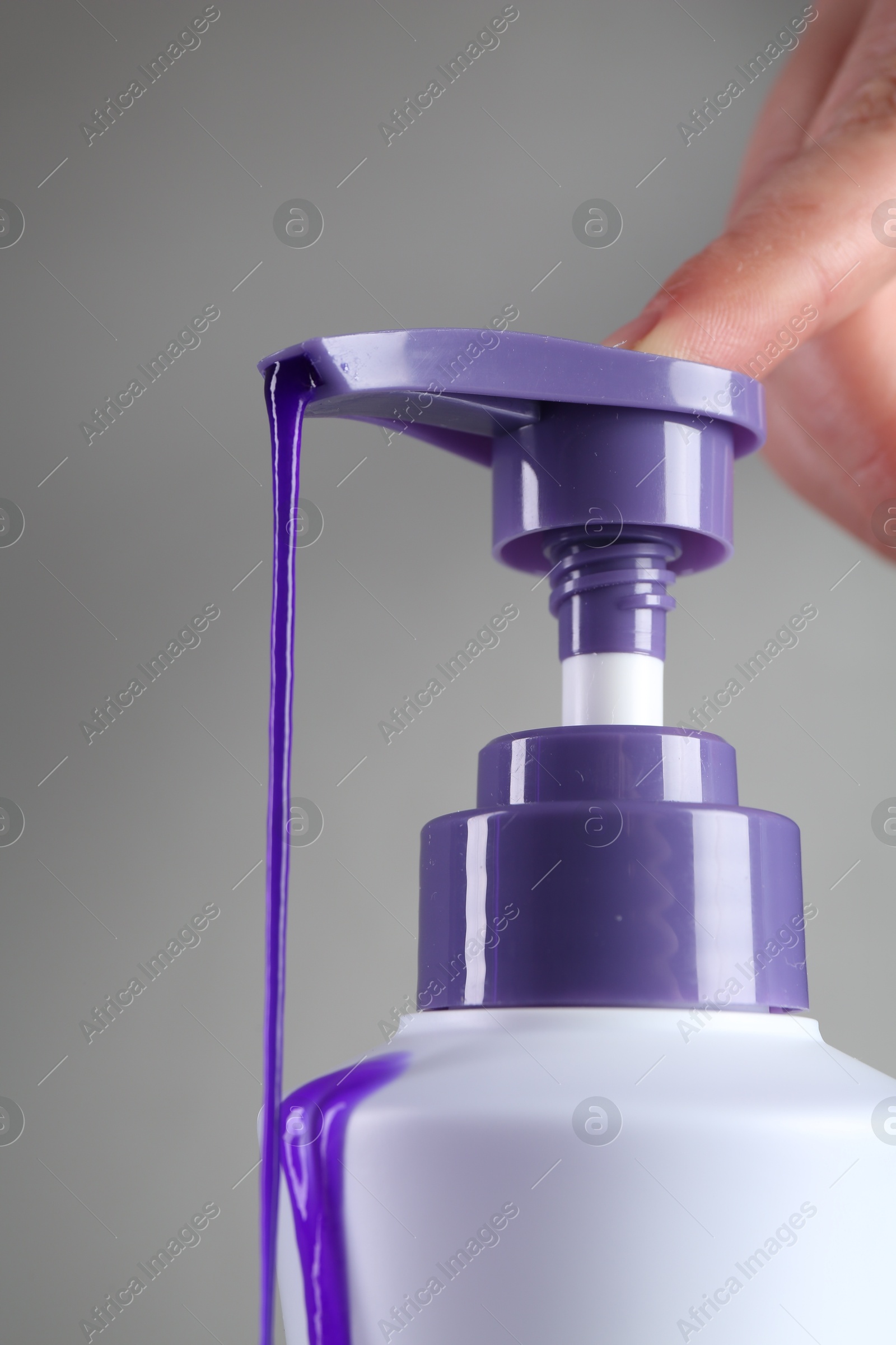 Photo of Woman with bottle of hair care product for blonde hair on grey background, closeup