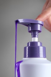 Photo of Woman with bottle of hair care product for blonde hair on grey background, closeup
