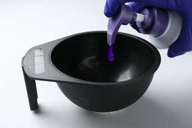Photo of Woman pouring hair care product for blonde hair from bottle into bowl on white background, closeup