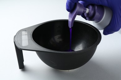 Photo of Woman pouring hair care product for blonde hair from bottle into bowl on white background, closeup