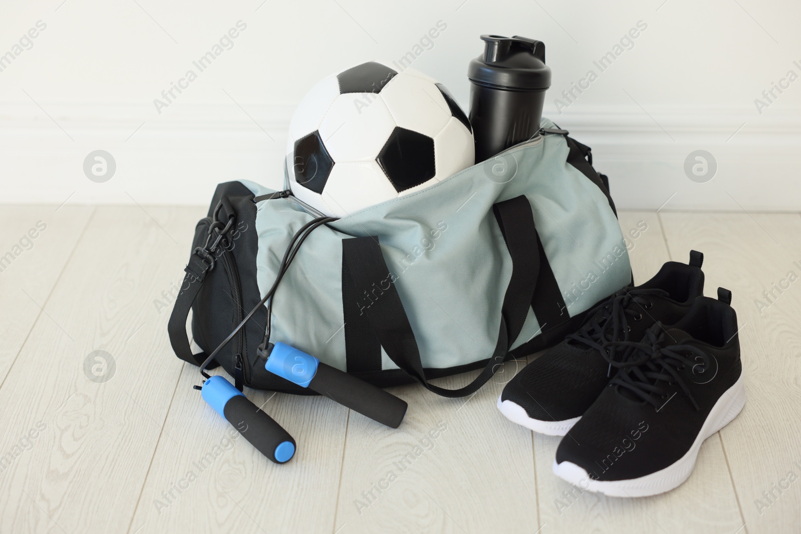 Photo of Stylish bag with sports equipment on floor indoors