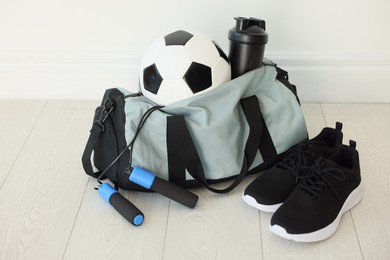 Photo of Stylish bag with sports equipment on floor indoors