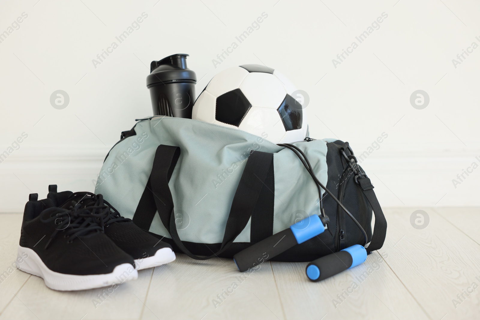 Photo of Stylish bag with sports equipment on floor indoors