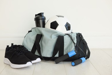 Photo of Stylish bag with sports equipment on floor indoors