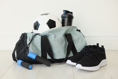 Photo of Stylish bag with sports equipment on floor indoors