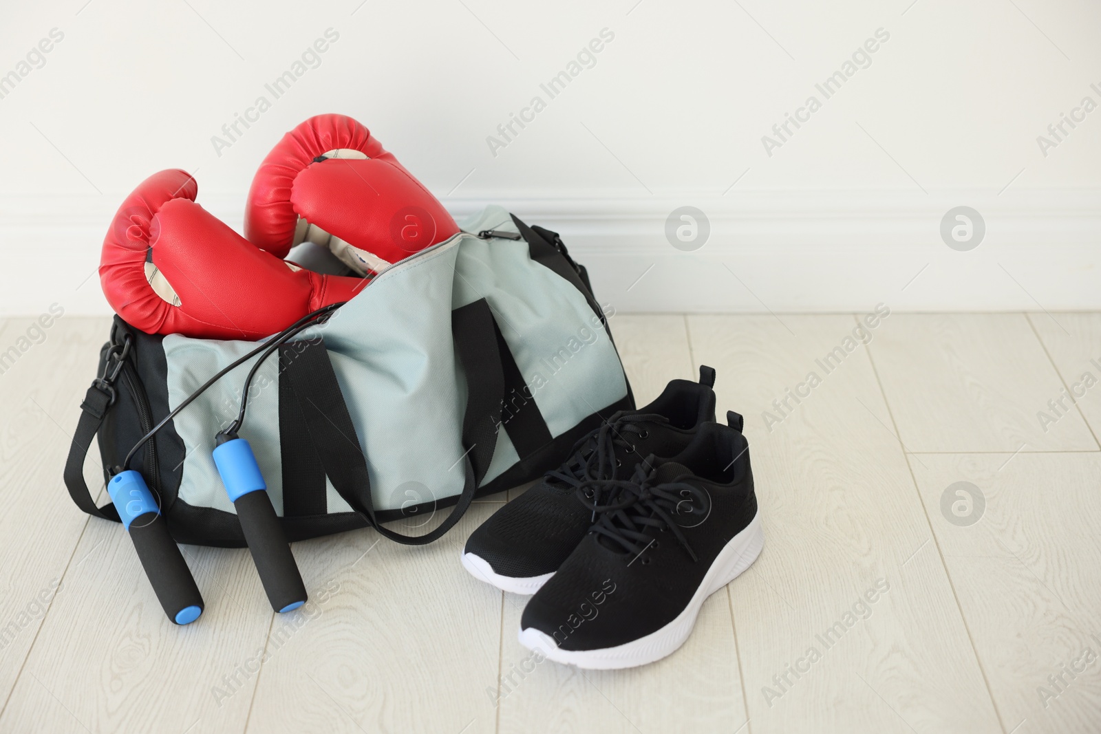 Photo of Stylish bag with sports equipment on floor indoors. Space for text